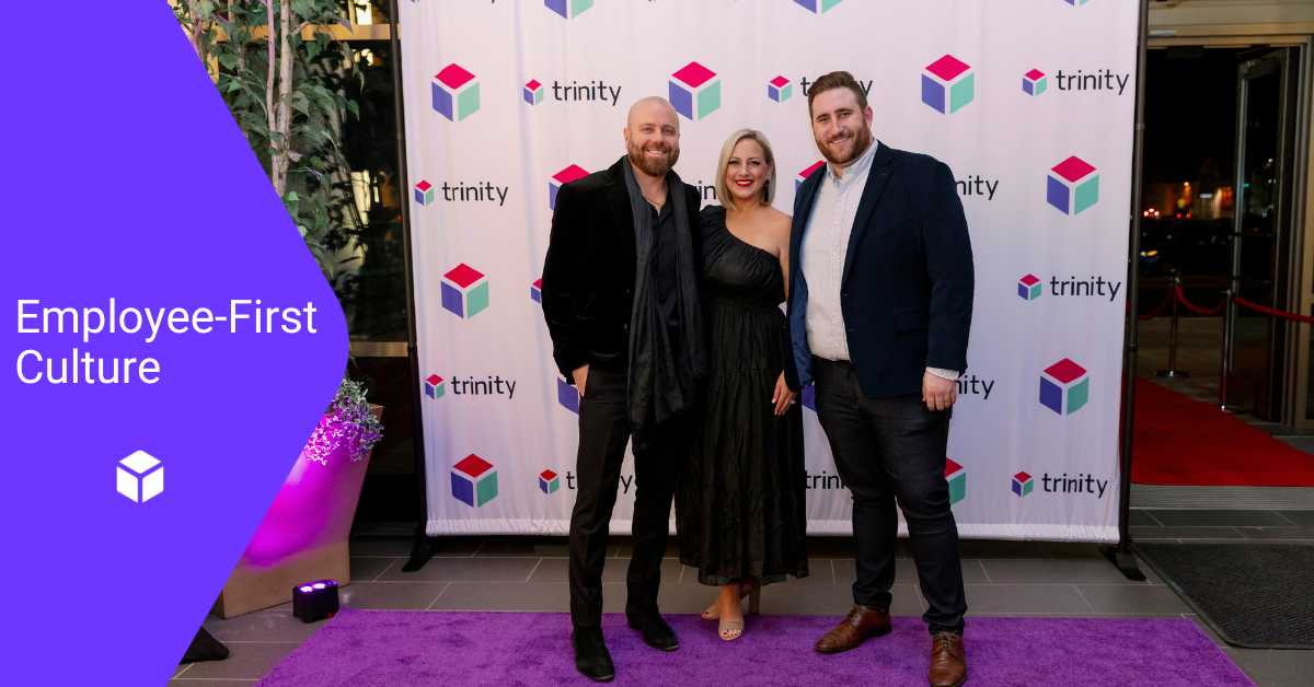 Trinity's CEO, VP of Customer Service, and General Manager pose in front of a Trinity-branded step and repeat